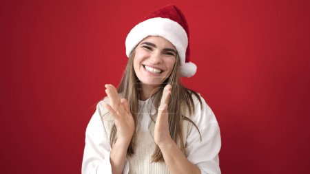 Téléchargez les photos : Jeune belle femme hispanique portant chapeau de Noël applaudissements mains sur fond rouge isolé - en image libre de droit
