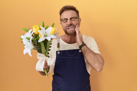 Photo for Middle age man with beard florist shop holding flowers touching mouth with hand with painful expression because of toothache or dental illness on teeth. dentist concept. - Royalty Free Image