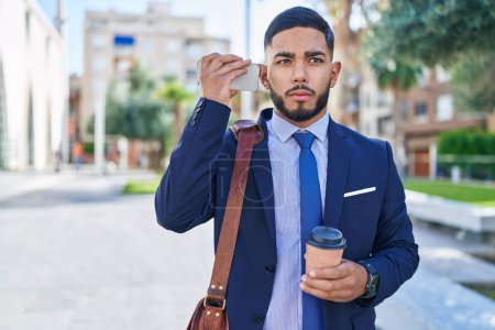 Téléchargez les photos : Jeune homme d'affaires latino écoute message vocal par smartphone boire du café au parc - en image libre de droit