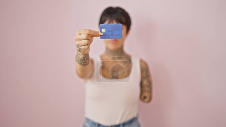 Téléchargez les photos : Femme hispanique avec bras amputé tenant la carte de crédit sur fond rose isolé - en image libre de droit