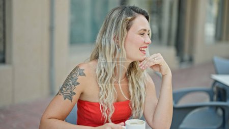Photo for Young blonde woman drinking coffee sitting on table smiling at coffee shop terrace - Royalty Free Image