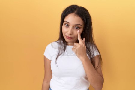 Photo for Young arab woman wearing casual white t shirt over yellow background pointing to the eye watching you gesture, suspicious expression - Royalty Free Image