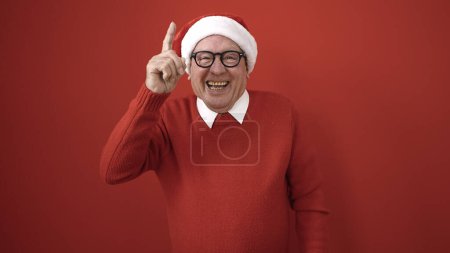Téléchargez les photos : Senior souriant faire geste idée avec doigt sur fond rouge isolé - en image libre de droit