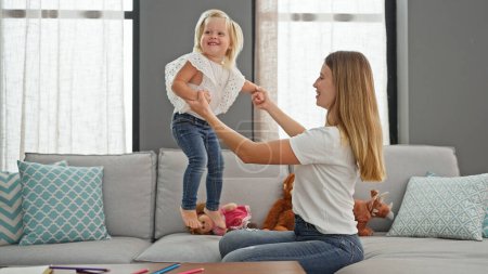 Photo for Confident caucasian mother and daughter bonding over giggles while jumping on sofa, radiating joy at their relaxing home - Royalty Free Image