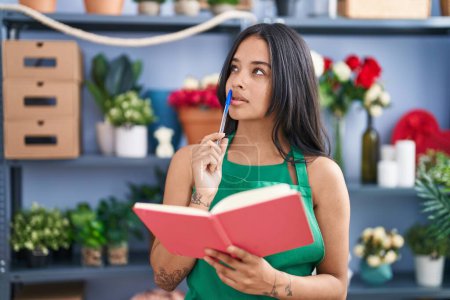 Téléchargez les photos : Young hispanic woman florist reading book at florist shop - en image libre de droit