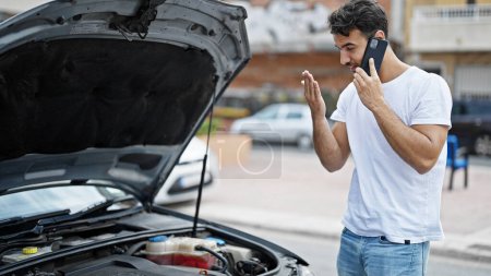 Téléchargez les photos : Jeune homme hispanique parlant sur smartphone avec assurance pour panne de voiture à la rue - en image libre de droit