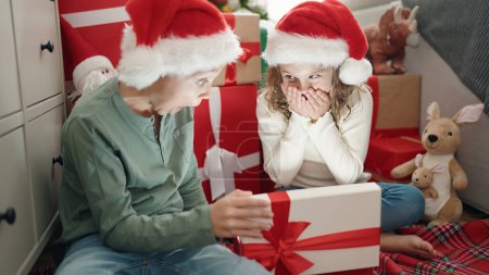 Téléchargez les photos : Deux enfants déballer cadeau assis sur le sol par arbre de Noël à la maison - en image libre de droit