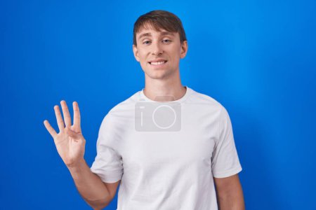 Photo for Caucasian blond man standing over blue background showing and pointing up with fingers number four while smiling confident and happy. - Royalty Free Image