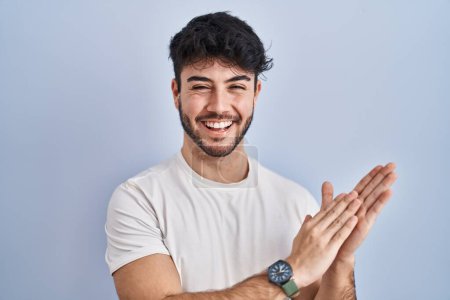 Foto de Hispanic man with beard standing over white background clapping and applauding happy and joyful, smiling proud hands together - Imagen libre de derechos
