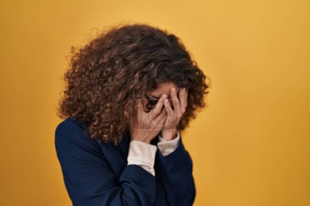 Photo for Hispanic woman with curly hair standing over yellow background with sad expression covering face with hands while crying. depression concept. - Royalty Free Image