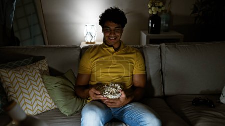 Téléchargez les photos : Jeune homme latino regardant un film assis sur un canapé à la maison - en image libre de droit