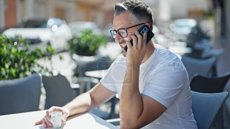 Téléchargez les photos : Homme aux cheveux gris buvant du café en parlant sur smartphone à la terrasse du café - en image libre de droit