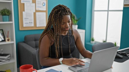 Foto de Trabajadora de negocios afroamericana usando laptop sonriendo en la oficina - Imagen libre de derechos