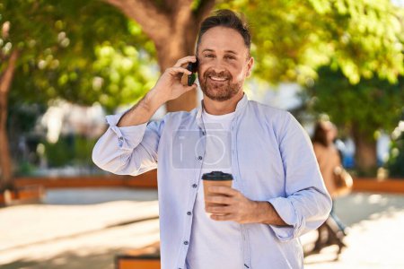Téléchargez les photos : Jeune homme caucasien parlant sur le smartphone boire du café au parc - en image libre de droit