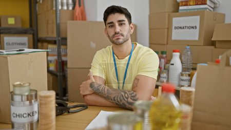 Téléchargez les photos : Jeune homme hispanique volontaire assis avec les bras croisés geste au centre de charité - en image libre de droit