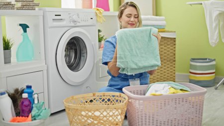 Téléchargez les photos : Jeune femme blonde nettoyant professionnel odeur serviette propre à la buanderie - en image libre de droit