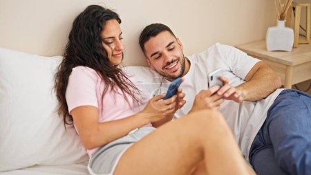 Téléchargez les photos : Homme et femme couple couché sur le lit en utilisant des smartphones dans la chambre - en image libre de droit