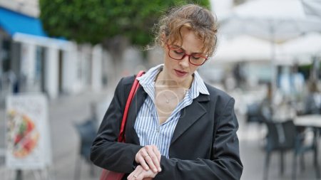 Téléchargez les photos : Jeune femme ouvrière regardant la montre avec un visage sérieux à la terrasse du café - en image libre de droit