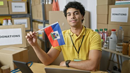 Photo for Young latin man volunteer holding haiti flag smiling at charity center - Royalty Free Image