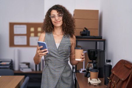 Téléchargez les photos : Jeune belle hispanique femme d'affaires en utilisant smartphone boire du café au bureau - en image libre de droit