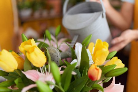 Téléchargez les photos : Jeune femme blonde fleuriste arrosage plante à la boutique de fleurs - en image libre de droit
