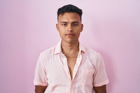 Téléchargez les photos : Jeune homme hispanique debout sur fond rose détendu avec une expression sérieuse sur le visage. simple et naturel regardant la caméra. - en image libre de droit