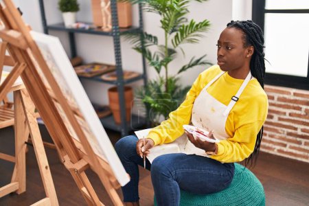 Foto de African american woman artist drawing with doubt expression at art studio - Imagen libre de derechos