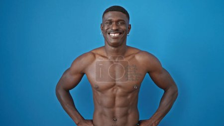 Foto de Hombre afroamericano sonriendo confiado de pie sin camisa sobre fondo azul aislado - Imagen libre de derechos
