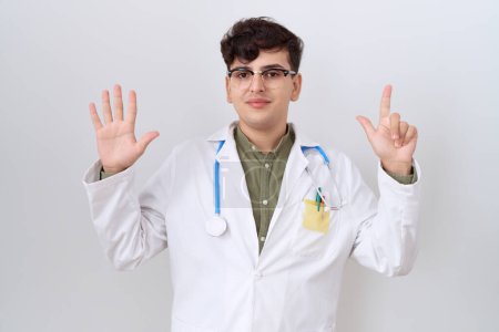 Téléchargez les photos : Jeune homme non binaire portant l'uniforme de médecin et stéthoscope montrant et pointant vers le haut avec les doigts numéro sept tout en souriant confiant et heureux. - en image libre de droit