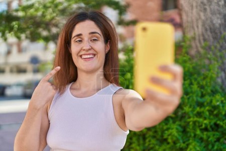 Téléchargez les photos : Femme brune prenant une photo selfie avec smartphone souriant heureux pointant avec la main et le doigt - en image libre de droit