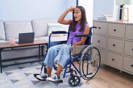 Photo for Young hispanic woman sitting on wheelchair at home very happy and smiling looking far away with hand over head. searching concept. - Royalty Free Image