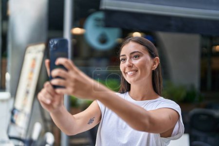 Téléchargez les photos : Young beautiful hispanic woman smiling confident making selfie by the smartphone at coffee shop terrace - en image libre de droit
