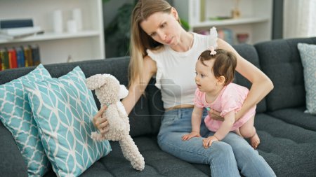 Photo for Mother and daughter sitting on sofa playing with teddy bear at home - Royalty Free Image