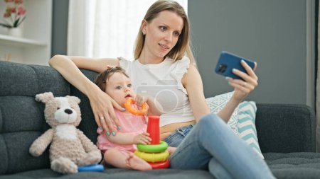 Photo for Mother and daughter watching video on smartphone while playing with hoops at home - Royalty Free Image