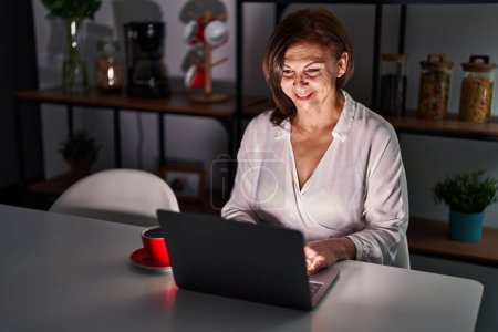 Photo for Middle age hispanic woman using laptop at home at night with a happy and cool smile on face. lucky person. - Royalty Free Image