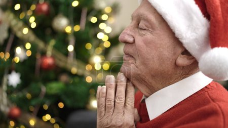 Photo for Senior praying sitting by christmas tree at home - Royalty Free Image