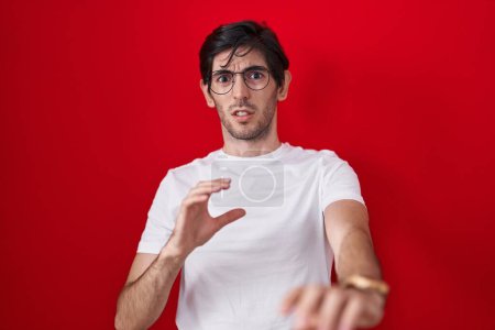 Photo for Young hispanic man standing over red background disgusted expression, displeased and fearful doing disgust face because aversion reaction. - Royalty Free Image