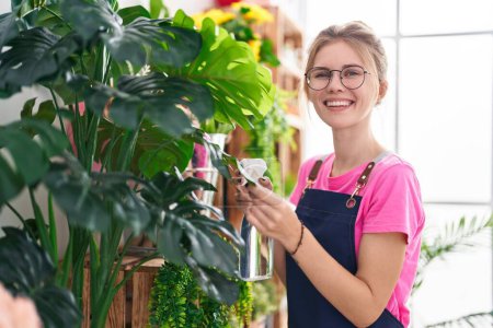 Téléchargez les photos : Jeune femme blonde fleuriste en utilisant diffuseur de travail souriant à la boutique de fleurs - en image libre de droit