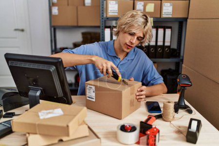 Téléchargez les photos : Jeune homme blond commerce électronique travailleur d'affaires déballage boîte en carton au bureau - en image libre de droit