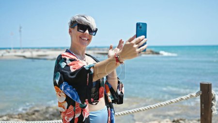 Foto de Joven turista con bikini y gafas de sol haciendo videollamadas en la playa - Imagen libre de derechos