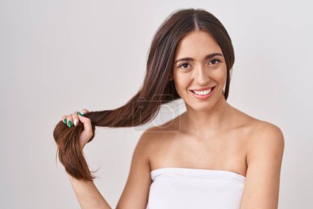 Téléchargez les photos : Jeune femme hispanique tenant les cheveux avec la main regardant positif et heureux debout et souriant avec un sourire confiant montrant les dents - en image libre de droit