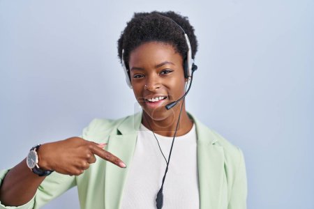 Téléchargez les photos : Femme afro-américaine portant casque agent du centre d'appel regardant confiant avec le sourire sur le visage, se montrant du doigt fier et heureux. - en image libre de droit