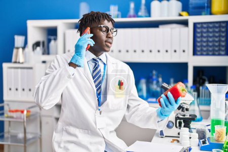 Téléchargez les photos : Un scientifique afro-américain parle sur un smartphone tenant du poivre au laboratoire - en image libre de droit
