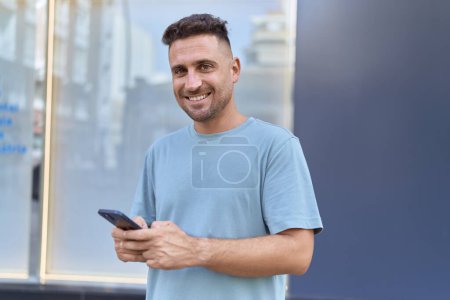Photo for Young hispanic man smiling confident using smartphone at street - Royalty Free Image