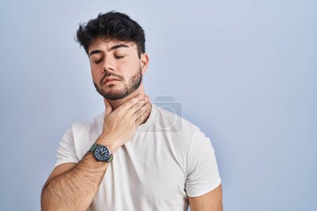 Foto de Hombre hispano con barba de pie sobre fondo blanco tocando el cuello doloroso, dolor de garganta por gripe, clod e infección - Imagen libre de derechos