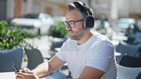 Téléchargez les photos : Homme aux cheveux gris écoutant de la musique assis sur la table à la terrasse du café - en image libre de droit