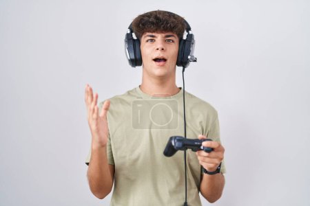 Photo for Hispanic teenager playing video game holding controller crazy and mad shouting and yelling with aggressive expression and arms raised. frustration concept. - Royalty Free Image