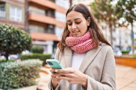 Photo for Young beautiful hispanic woman using smartphone wearing scarf at park - Royalty Free Image
