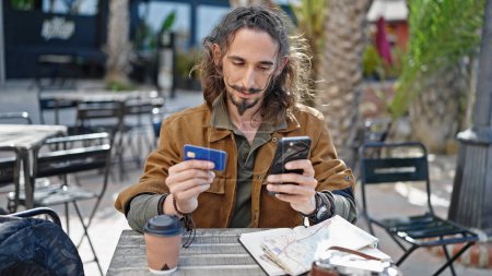 Foto de Joven turista hispano usando teléfono inteligente sentado en la mesa en la terraza de la cafetería - Imagen libre de derechos