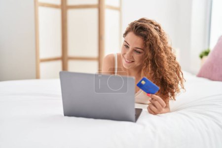Foto de Young beautiful hispanic woman using laptop and credit card sitting on bed at bedroom - Imagen libre de derechos